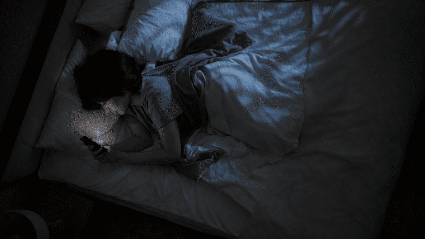 暗い寝室でベッドに横になって休む人（スマホを手にしている）